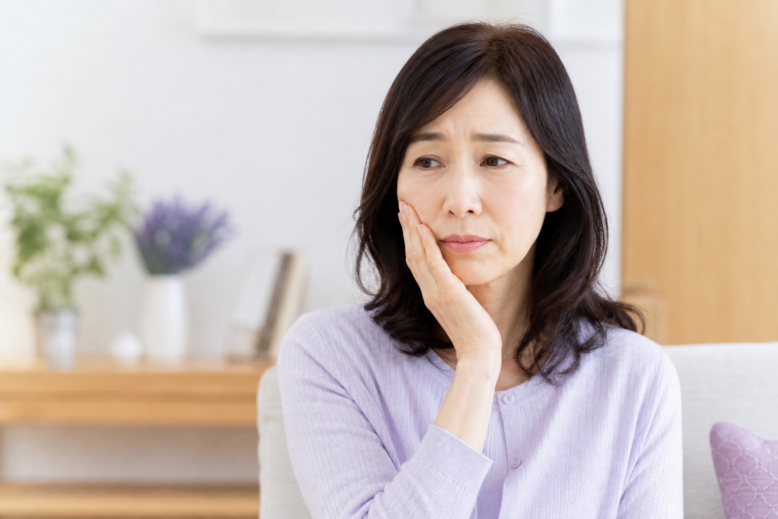 虫歯の痛みで頬を押さえ、困った表情を見せる女性